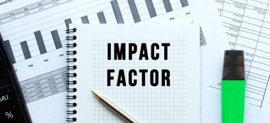 IMPACT FACTOR 'u ofis masasındaki mali tabloların üzerinde duran bir not defterinin sayfasına yaz. Hesap makinesinin yanında. İş konsepti.