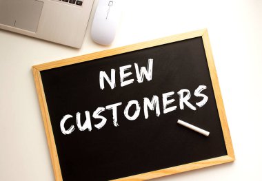 Tahtaya tebeşirle yazılmış YENİ CUSTOMERS metni. Ofis masası İş konsepti.