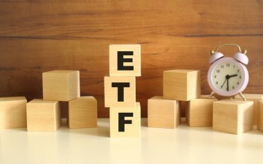 Kahverengi arka planda dikey olarak dizilmiş üç tahta küp ETF sözcüğünü oluşturuyor. Küpler yakınlarda ve bir saat var. Ön Görünüm Kavramları