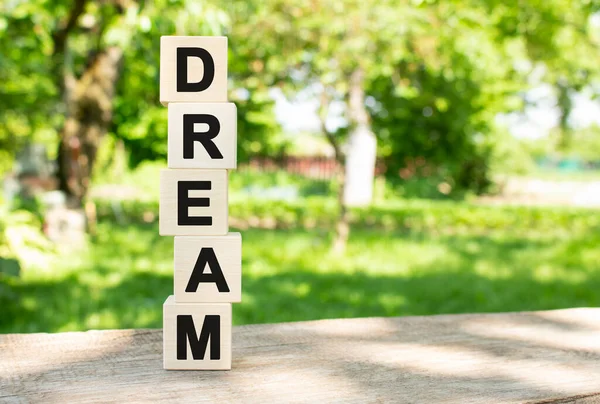 Tahta küpleri dikey olarak bahçedeki ahşap bir masanın üzerine istiflenmiştir. DREAM kelimesi siyah harflerle yazılır. Tasarımınız için kavram