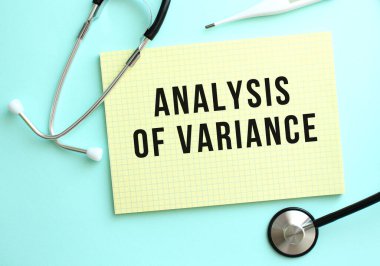 VARIANCE ANALYSIS metni mavi arkaplanda steteskopun yanında duran sarı bir deftere yazılmıştır. Tıbbi konsept