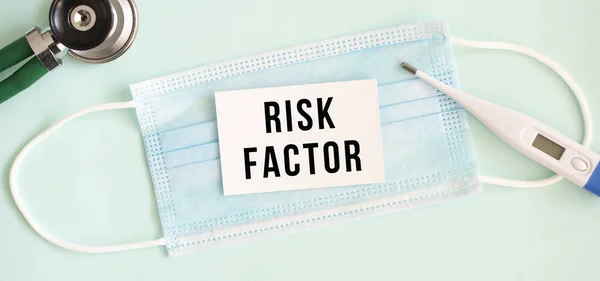 White card with the inscription RISK FACTOR on a medical protective mask. Medical concept.