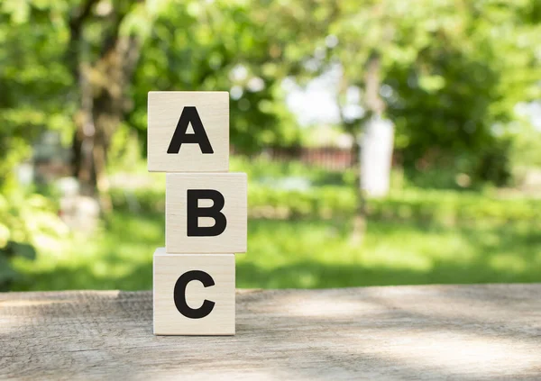 Wooden cubes are stacked vertically on a wooden table in the garden. The word ABC is written in black letters. Concept for your design
