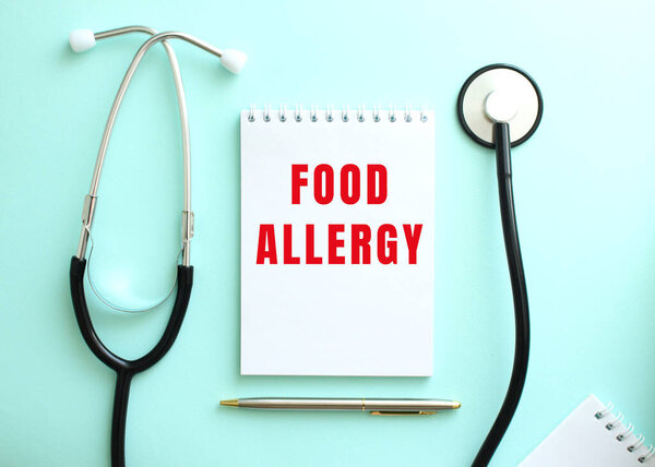 On a blue background, a stethoscope and a white notepad with the red words FOOD ALLERGY. Medical concept