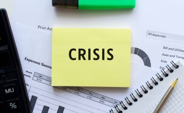 Ofis masasındaki mali tabloların üzerinde duran not defterinin sayfasına CRISIS 'i yaz. Hesap makinesinin yanında. İş konsepti.