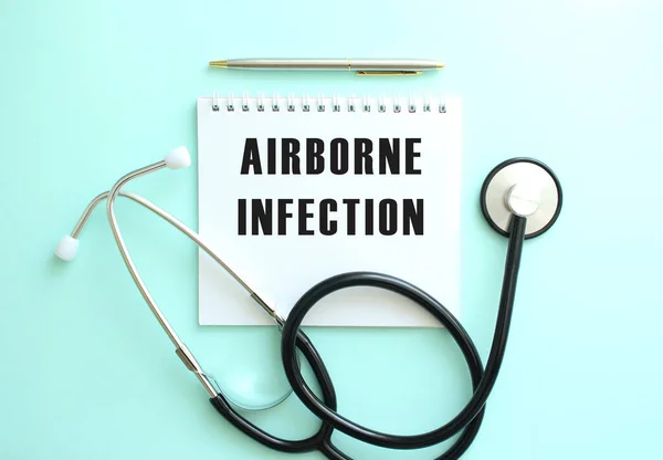 White notepad with the words AIRBORNE INFECTION and a stethoscope on a blue background. Medical concept