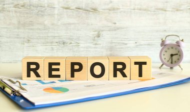 Wooden cubes lie on a folder with financial charts on a gray background. The cubes make up the word REPORT. Business concept.