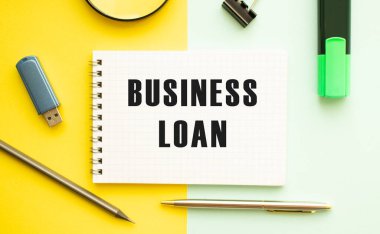 Ofis masasında ofis malzemeleriyle birlikte BUSINESS kredisinin olduğu defter. Sarı arkaplan kavramı. İş konsepti.