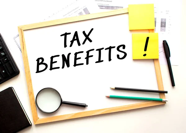 TAX BENEFITS text is written on a white office board. Work table with office supplies. Business and financial concept.