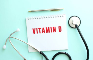 Kırmızı metin VITAMIN D ve steteskoplu beyaz not defteri mavi arkaplanda.