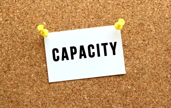 CAPACITY is written on a card attached to the corkboard with a button. Reminder on the office board. — Stock Photo, Image