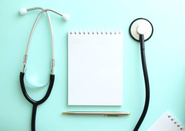 Mavi arka planda, steteskop ve beyaz bir not defteri var. Tıbbi konsept