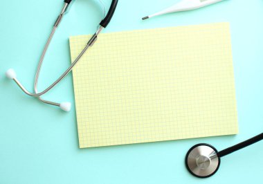 Mavi arka planda steteskopun yanında duran sarı defterdeki yazı için yer. Tıbbi konsept.