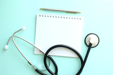 Mavi arka planda beyaz not defteri ve steteskop..