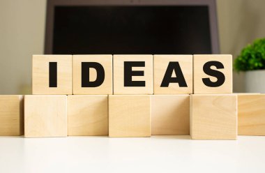 IDEAS kelimesi ofis masasında dizüstü bilgisayarın önünde duran tahta küplere yazılmıştır. İş konsepti.