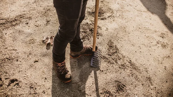 Boots stepping on the ground with hoe and rake for agriculture, ecologic farm work and gardening