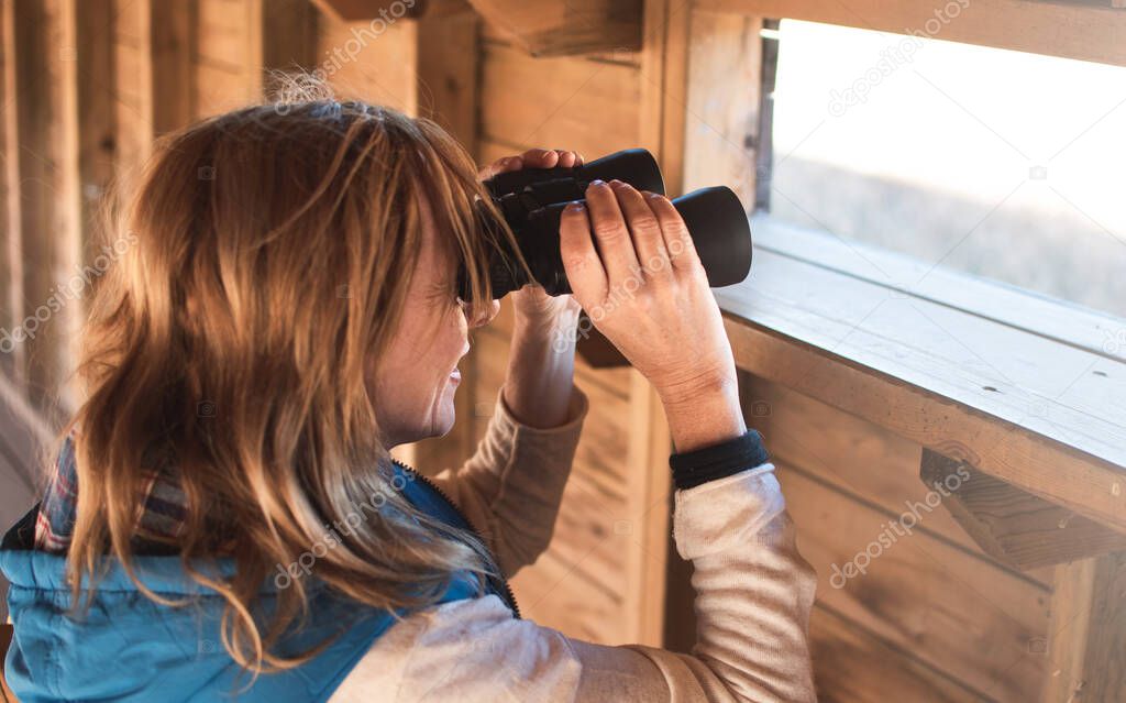 Girl in nature with binoculars doing outdoors activities . Searching, sightseeing , tourism, discover and birdwatching concept.