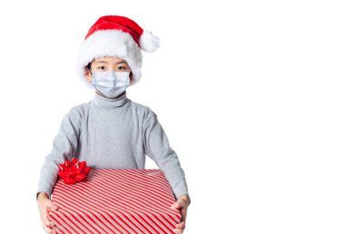 Covid Noel 'de Noel Baba şapkası ve maskesi takan küçük bir çocuk, salgın nedeniyle beyaz arka planda izole edilmiş ve fotokopi alanı olan Noel Baba maskesi takıyor..