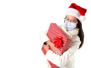 Covid Noel 'de Noel Baba şapkası ve maskesi takan genç bir kız, salgın yüzünden beyaz arka planda izole edilmiş ve fotokopi alanı olan Noel Baba şapkası takıyor..