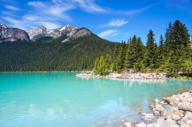 Unrecognizable visitors on the lakeshore of beautiful glacier-fed Lake Louise in Banff National Park with the Canadian Rockies in the background. 