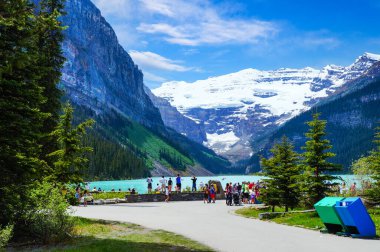 Unrecognizable visitors at glacier-fed Lake Louise in Banff National Park with snow covered famous Mount Victoria in the background. 