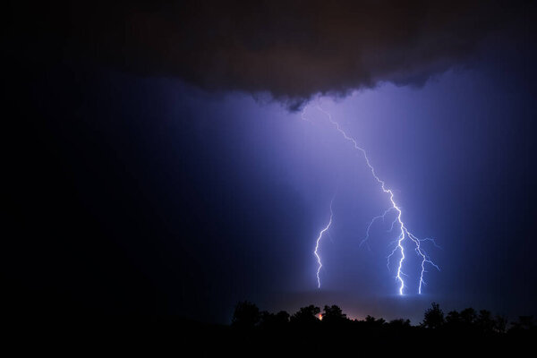 Three powerful lightning bolts during a night thunderstorm over the sea.