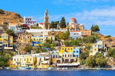 Mükemmel güneşli bir gün ve deniz manzarası Yunan adasındaki kayalıklarda renkli evler üzerinde Simi