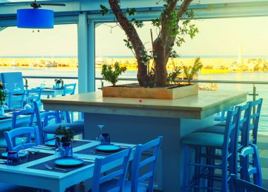 Tables and chairs at a waterfront bar with views across the harbour, Hersonissos, Crete, Greece