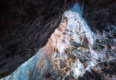 Mağaranın girişinin duvarları sarkıt ve yeşil bitki örtüsüyle kaplı.