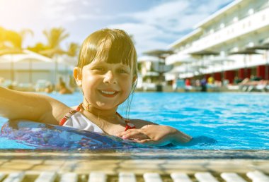 Mutlu çocuk havuzda otelin arka planında ve gökyüzünde bulutlarla oynuyor. Yaz tatili kavramı.