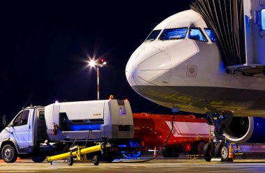 Gece havaalanında geniş gövdeli yolcu uçağı. Uçak burnu yakın. Yan görüş. Kalkıştan önce uçuş öncesi uçak servisi. Borda köprüsü uçakla kenetlendi..