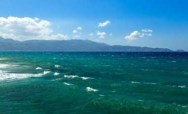 Parlak güneşli bir gün, kayalara ve bulutlara karşı dalgalı bir deniz, Avrupa, Girit, Yunanistan