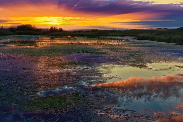 Untergehende Sonne zwischen Wolken auf einem See im Hintergrund mit Reflexion — Stockfoto