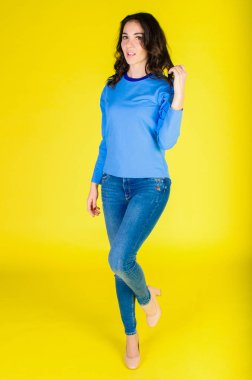 Mavi elbiseli bir model sarı arka planda poz veriyor.