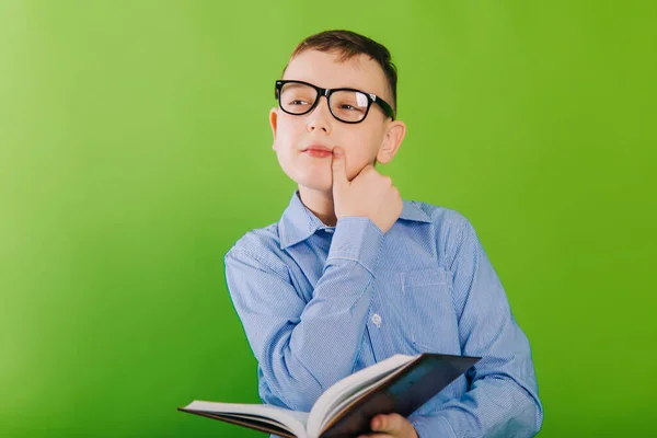 A boy in a blue striped shirt wears black glasses and reads a book. Child with poor eyesight teaches lessons. Gains knowledge at home.