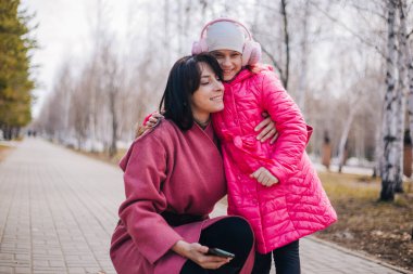 Anne ve kızı parkta selfie çekiyor. Çocuk kışın annesiyle yürür..