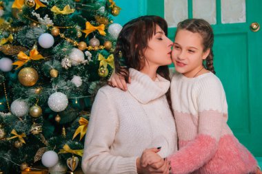 Anne ve kızı Noel kapısındaki merdivenlerde oturmuş yeni yılı bekliyorlar. Sevgi dolu bir aile, kızı öpüyor..