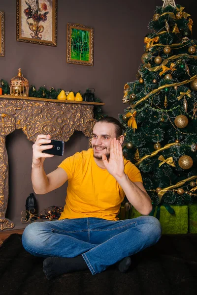 Happy Guy Yellow Shirt Sits Background Christmas Tree Holds Phone — Stock Photo, Image