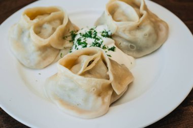 Ekşi krema ve bitkilerle dolu beyaz bir tabakta büyük bir manti. Doğu mutfağı. Hamurda et.