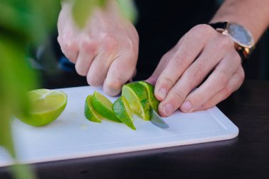 Erkek eli, bir kokteyl için yeşil kireç keser. Açık hava partisi.