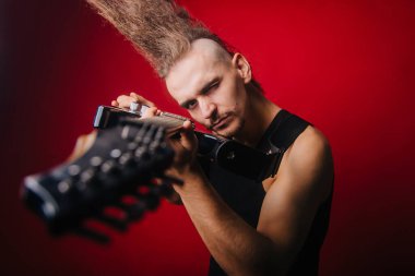 Siyah elektro gitarlı, bıyıklı ve büyük mohawklı bir serseri. Stüdyoda kırmızı arka planda rock müzisyeni var. Gayri resmi hareket