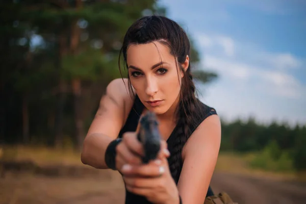 Girl with a gun in nature to aim at the enemy. Against the background of yellow grass. The female army on the hunt. Military action in a hot country