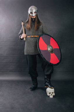 Viking gri bir arka planda baltayla duruyor. Zincirli zırhlı bir adam ve bir kask düşmanın kafasına bastı. Zırhlı ortaçağ savaşçısı. Stüdyo fotoğrafı