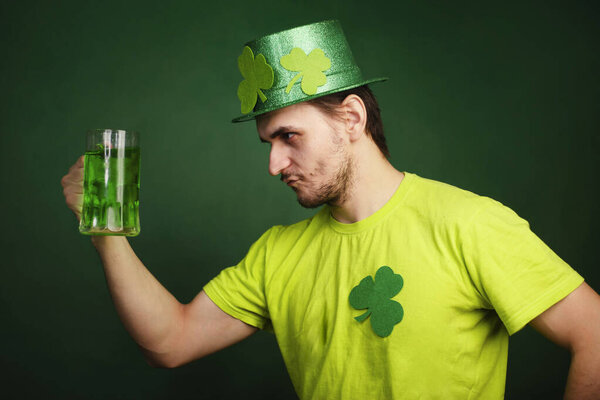 Мужчина в шляпе и зеленой футболке пьет большую кружку зеленого эля. Парень празднует День Святого Патрика с бокалом пива.