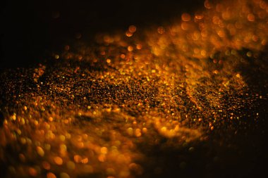 Pullardan altın kum. Siyah arka plana yayılmış ışıltılar. Bulanık bokeh arkaplanı
