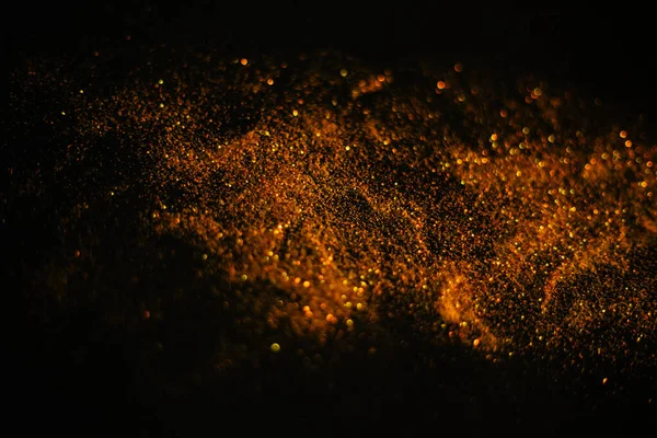 Gold sand from sequins. Scattered sparkles on a black background. Blurred bokeh background — Stock Photo, Image