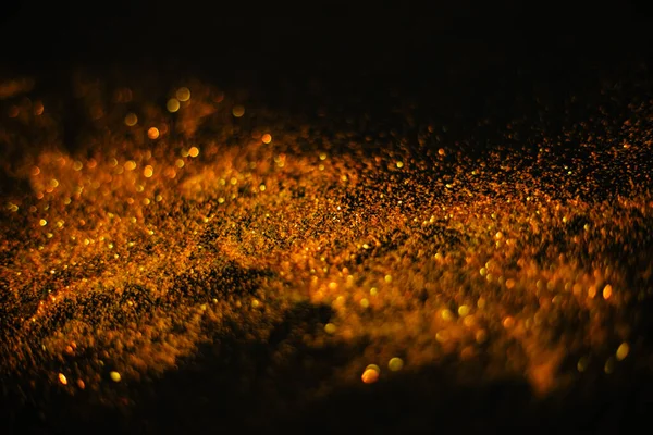 Złoty piasek z cekinów. Rozproszone iskry na czarnym tle. Niewyraźne tło bokeh — Zdjęcie stockowe