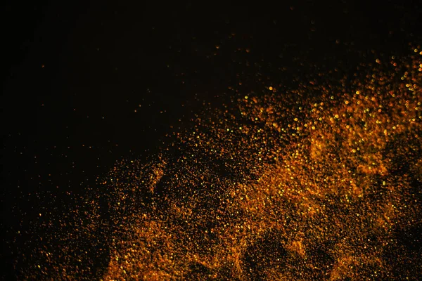 Goldsand aus Pailletten. Verstreut funkelt es auf schwarzem Hintergrund. Verschwommener Bokeh-Hintergrund — Stockfoto