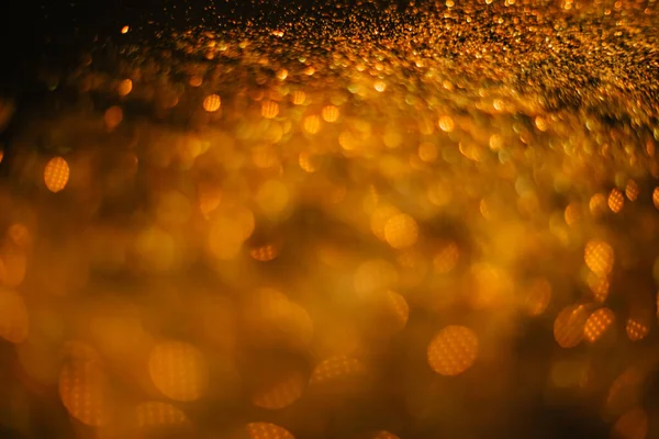 Gold sand from sequins. Scattered sparkles on a black background. Blurred bokeh background — Stock Photo, Image