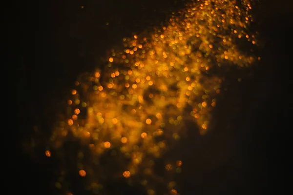 Gold sand from sequins. Scattered sparkles on a black background. Blurred bokeh background — Stock Photo, Image